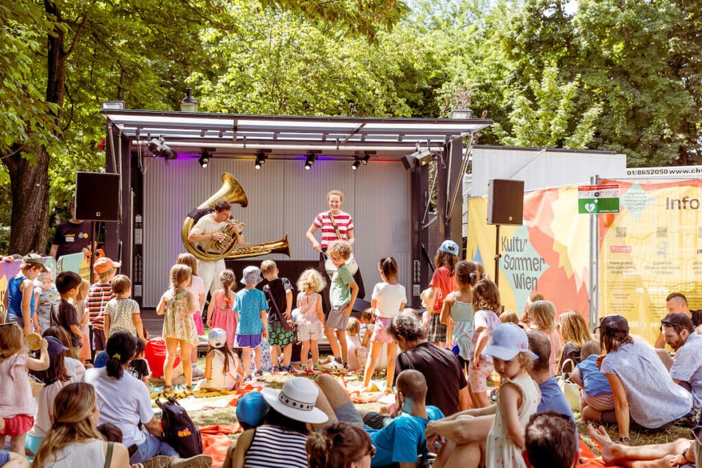 Zahlreiche Kinder und Familien genießen auf Picknickdecken das kostenlose Kinderprogramm beim Kultursommer Wien mit Musik.